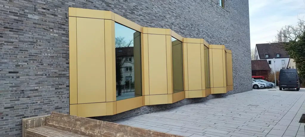 Goldfarbene Aluminiumkassetten und Einfassungen um mehrere Fenster eines Klinkergebäudes