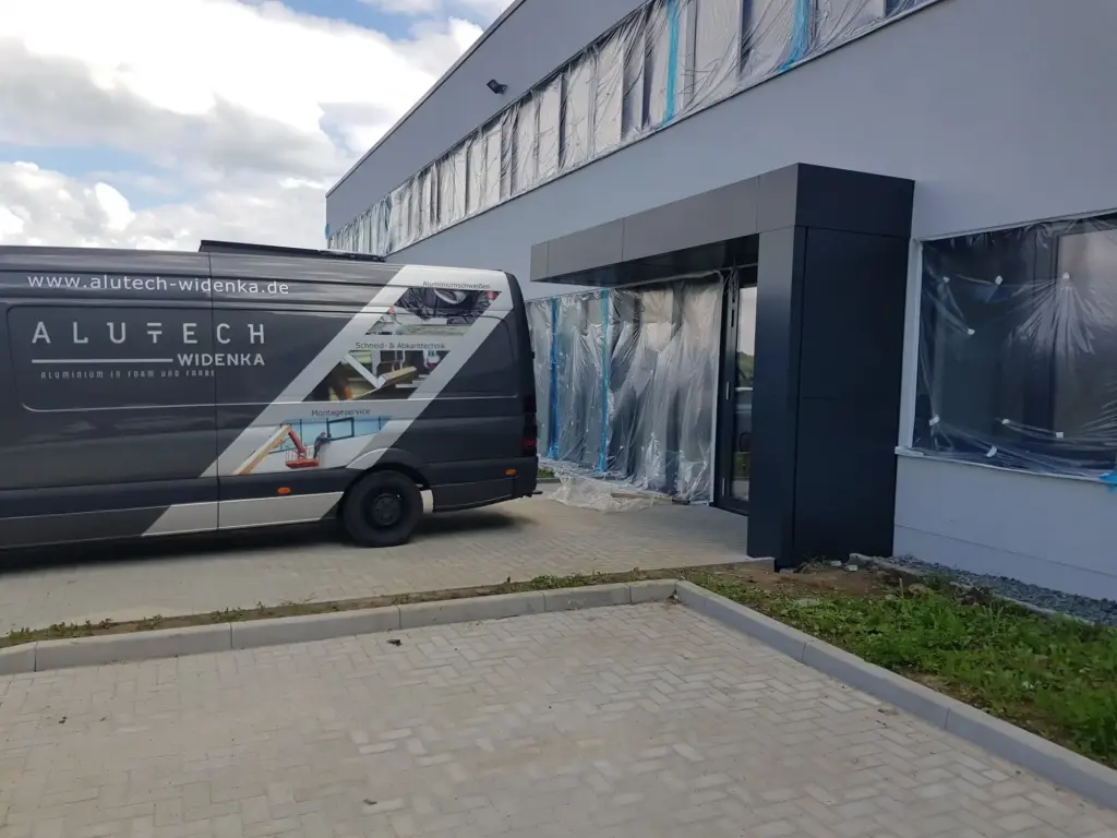 Beschriftetes Montagefahrzeug von Alutech Widenka vor einem verkleideten Eingangsbereich