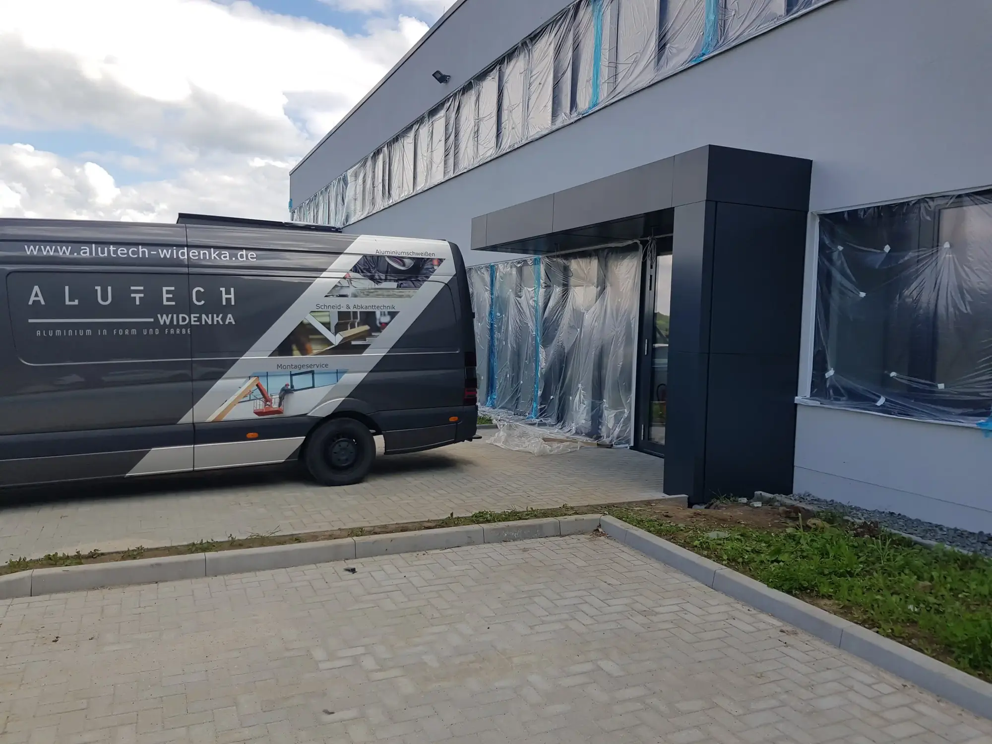 Beschriftetes Montagefahrzeug von Alutech Widenka vor einem verkleideten Eingangsbereich